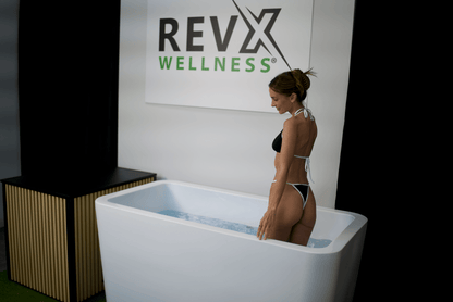 Woman standing next to a white soaking tub with 'REVX Wellness' branding in the background.